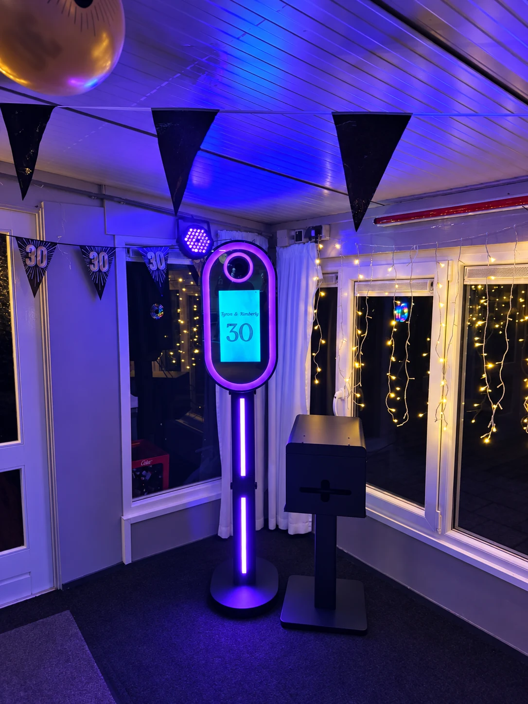 Paarse fotoboothverlichting tussen feestvlaggetjes en warme lichtjes.